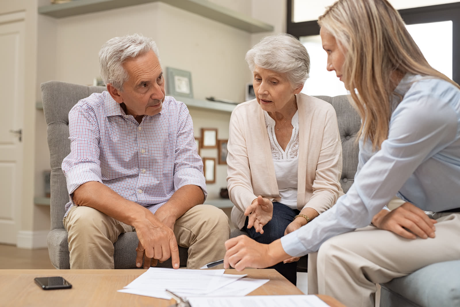 2026-09-what-damages-can-a-family-recover-florida-wrongful-death-case An older man and woman sit with a younger woman in a living room, leaning over printed documents spread on the coffee table between them.